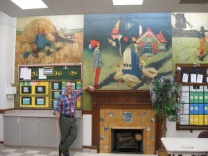 Photo by Sue Suchyta. Salina Intermediate School teacher Paul Bruce shows some of the Edward McCandlish Mother Goose nursery rhyme murals, created as part of a Depression-era Public Works of Arts Project, in what was once one of the school's kindergarten rooms, now used as a conference room. The paintings include “Little Boy Blue” (left), painted on two wooden panels, and “Mother Goose”. The hand-carved wooden fireplace mantel, original to the school's 1926 construction, features vintage Pewabic tile.