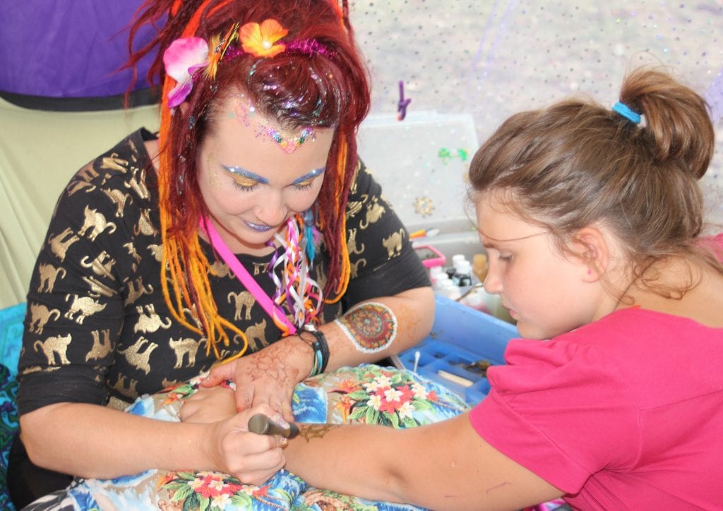 Facepaint Faerie Jamie Laakko (left) creates a temporary glitter tattoo for Olivia Sherwood, 9, of Lincoln Park.
